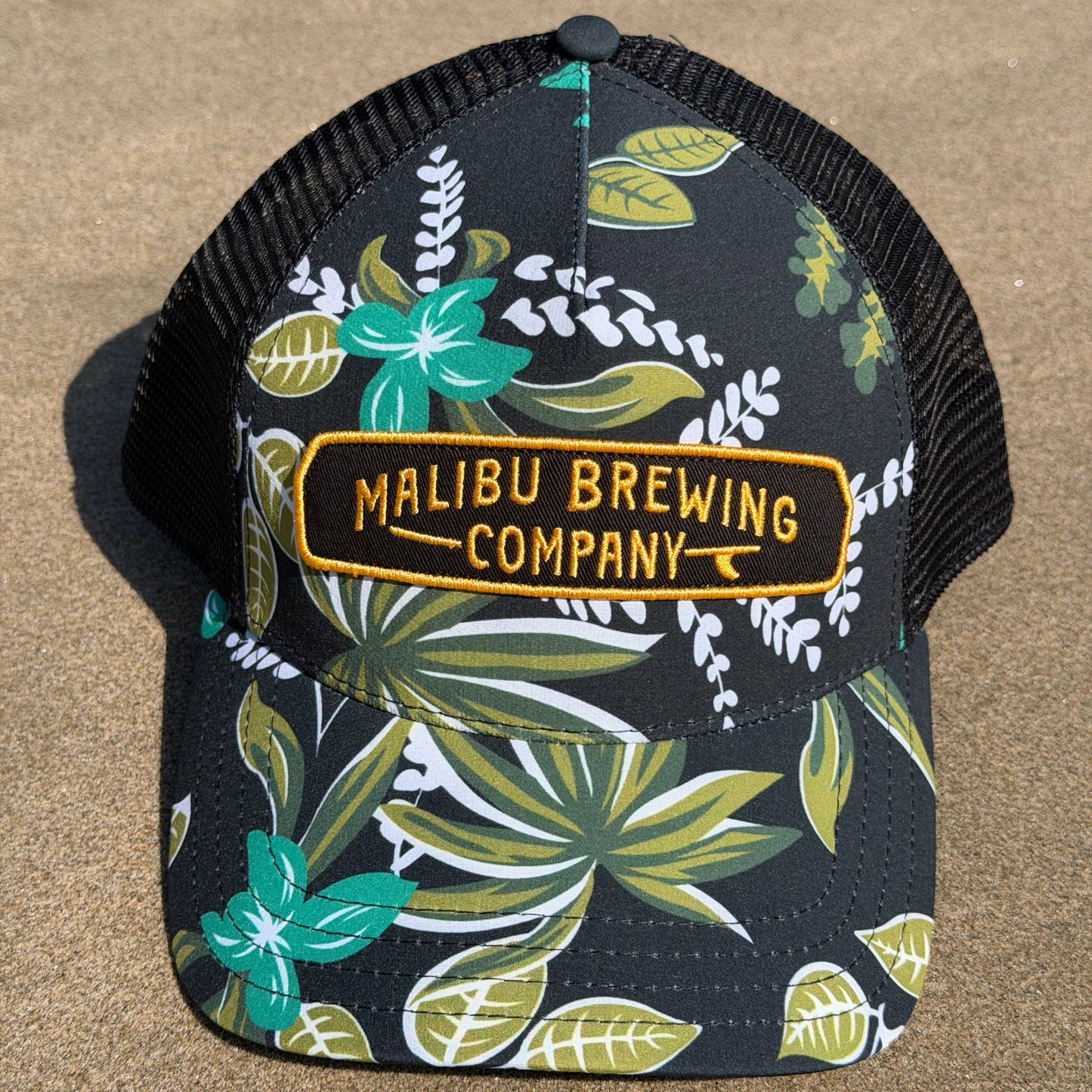 Floral-patterned coaster with Malibu Brewing Company logo on a beige surface