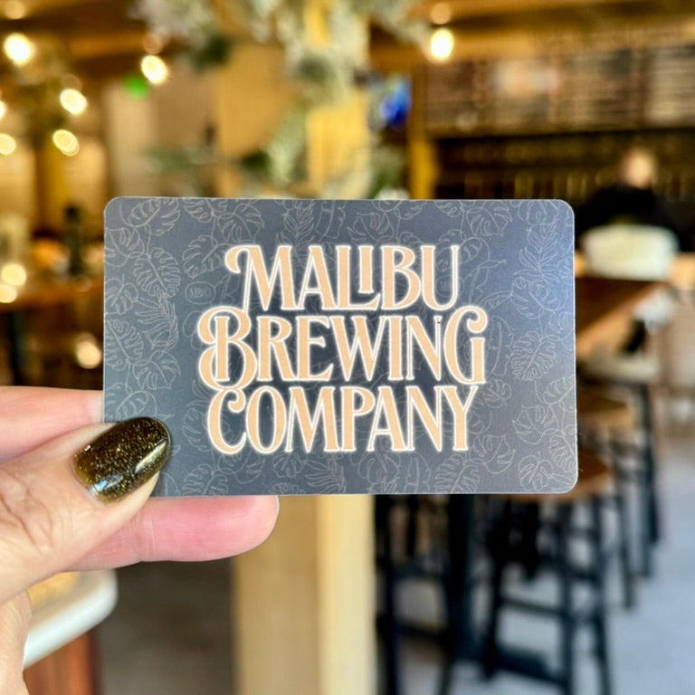 Malibu Brewing Company gift card held in front of a blurred bar setting