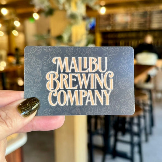Malibu Brewing Company gift card held in front of a blurred bar setting