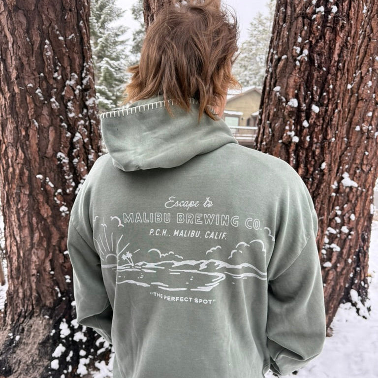 Person wearing a hoodie with a Malibu Brewing Co. logo in a snowy forest setting