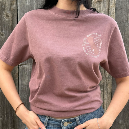 Person wearing a mauve t-shirt with a graphic design against a wooden background