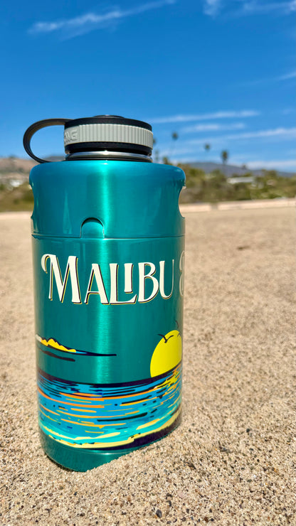 A Keg Growlers bottle in turquoise, featuring a Malibu beach sunset design, stands upright on sandy beach beneath a blue sky scattered with clouds and distant palm trees—its stylish 64oz stainless construction perfect for keeping your drinks cold during any coastal adventure.