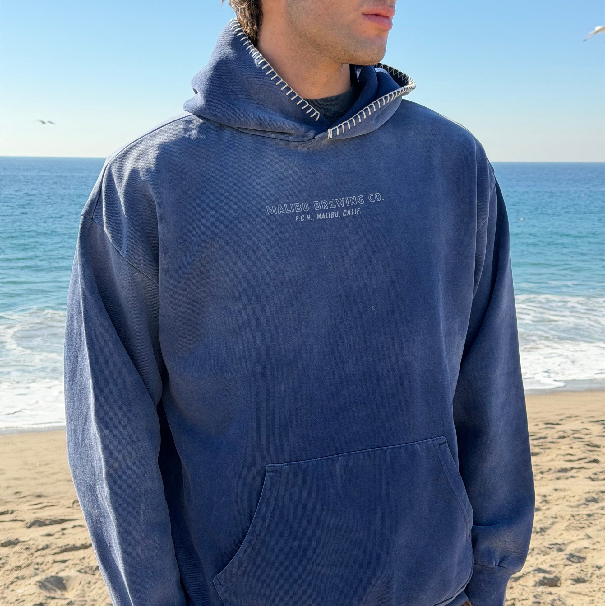 Person wearing a blue hoodie with text on a beach