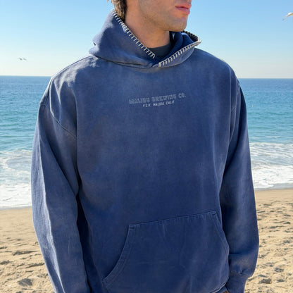 Person wearing a blue hoodie with text on a beach