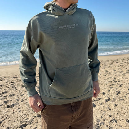 Person wearing a green hoodie with text on a beach